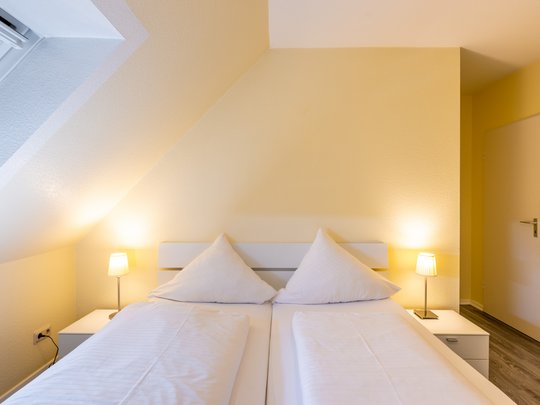 Ihre Unterkunft in Gemünd – Eifel-Urlaub voller Freiheit Gemütliches Schlafzimmer mit Doppelbett, weißen Kissen und zwei Nachttischlampen