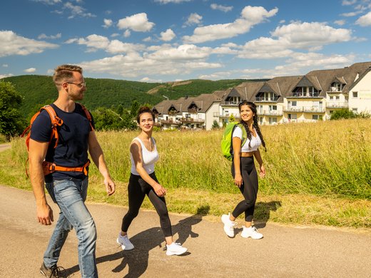 Holiday apartments in Gemünd with special flair Three young people hiking on sunny path with holiday park in the background