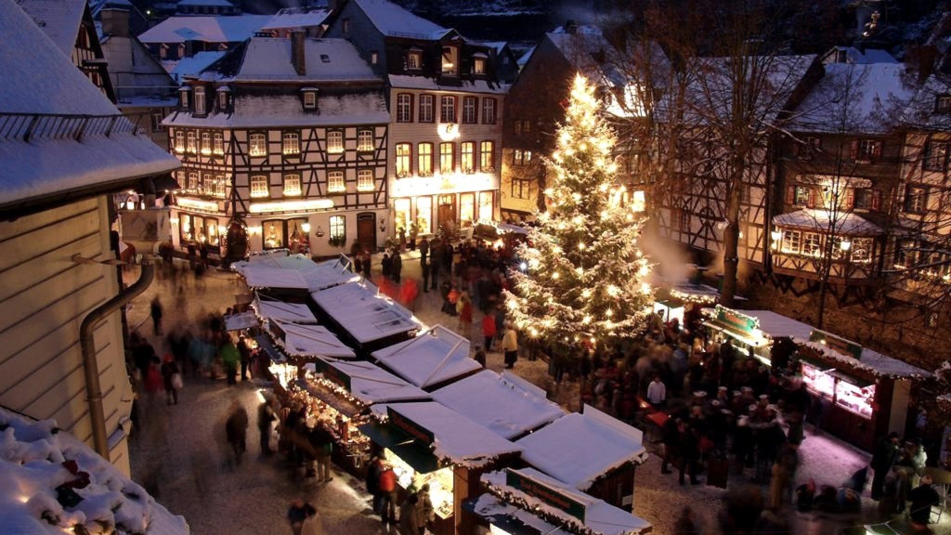 Eifel-Urlaub: Weihnachtsmärkte der Region Weihnachtsmarkt mit beleuchtetem Baum und verschneiten Fachwerkhäusern bei Nacht