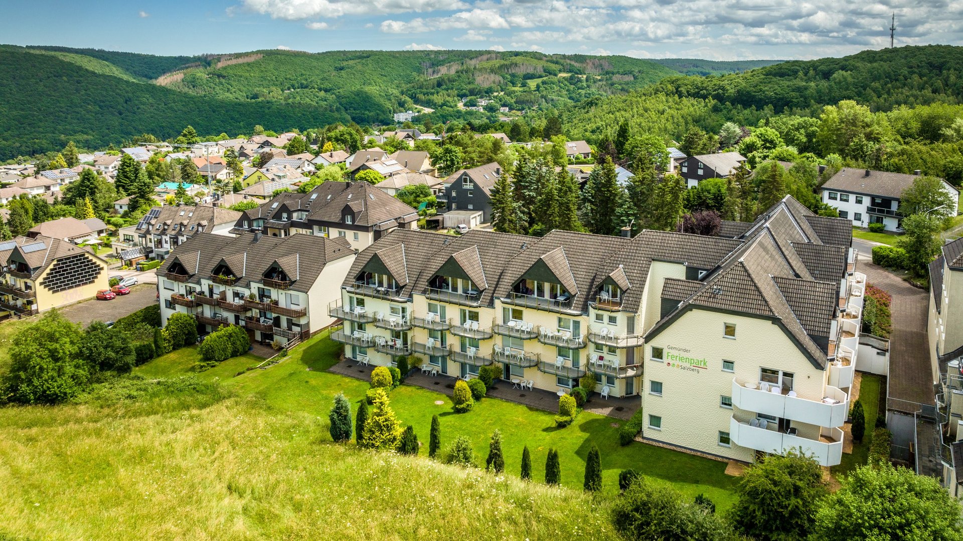 Holiday apartments in Gemünd with special flair View of holiday park with houses and green hills under a blue sky