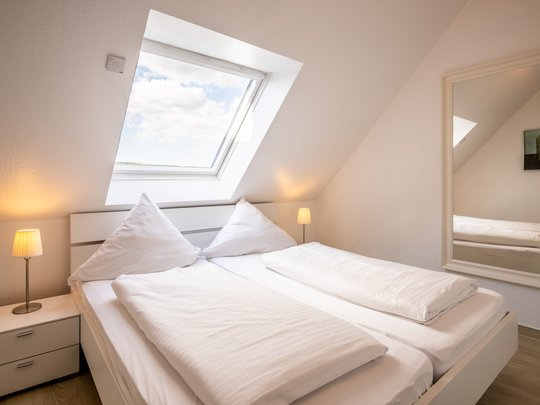 Ihre Unterkunft in Gemünd – Eifel-Urlaub voller Freiheit Helles Schlafzimmer mit Dachfenster, Doppelbett und Nachttischen mit Lampen