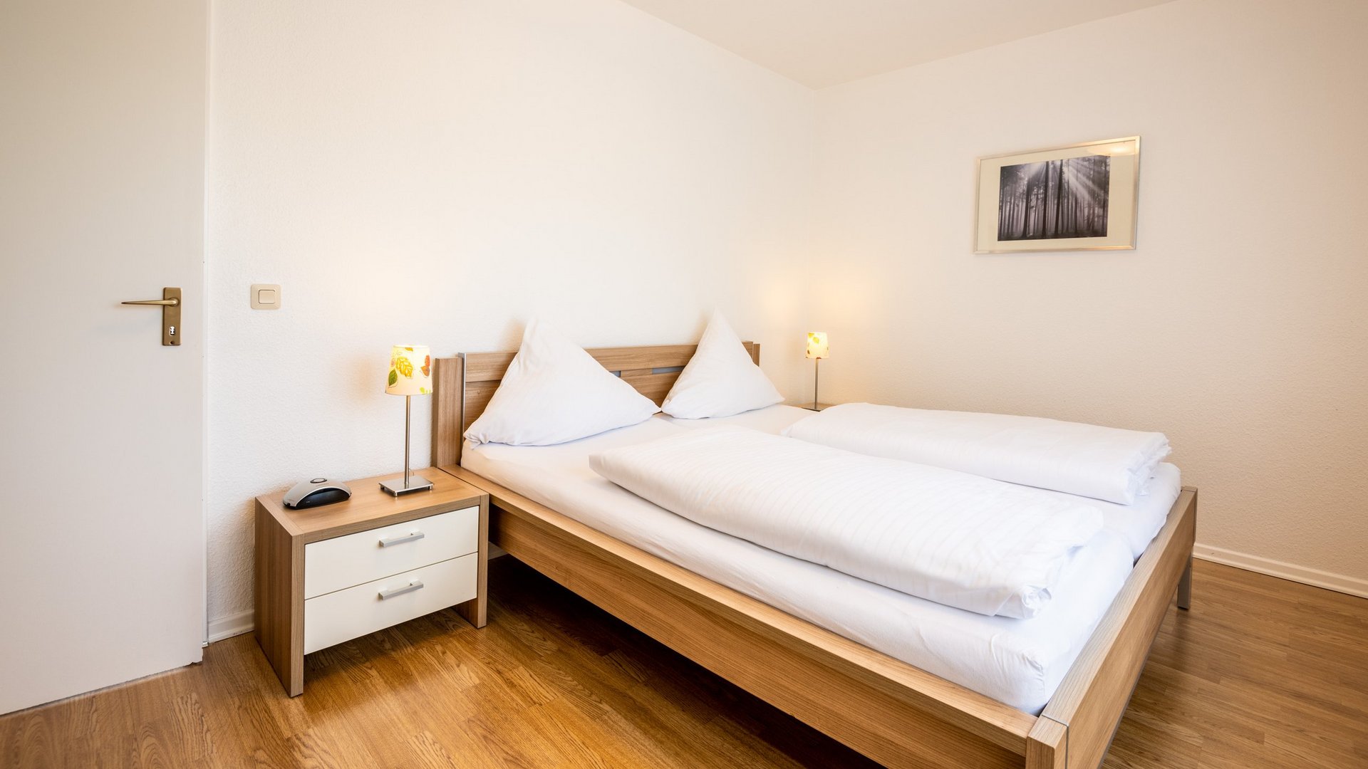 Ihre Unterkunft in Gemünd – Eifel-Urlaub voller Freiheit Helles Schlafzimmer mit Doppelbett, Nachttisch und Lampen