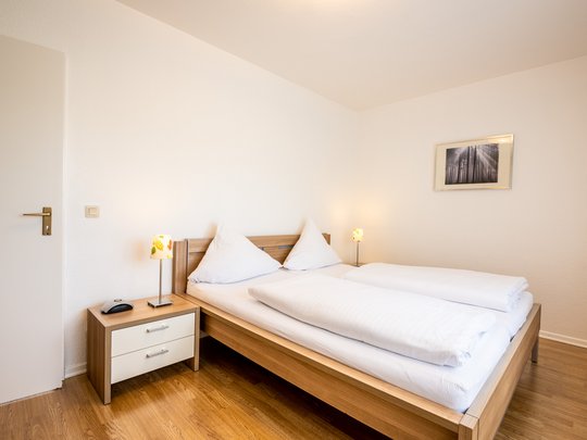 Ihre Unterkunft in Gemünd – Eifel-Urlaub voller Freiheit Helles Schlafzimmer mit Doppelbett, Nachttisch und Lampen