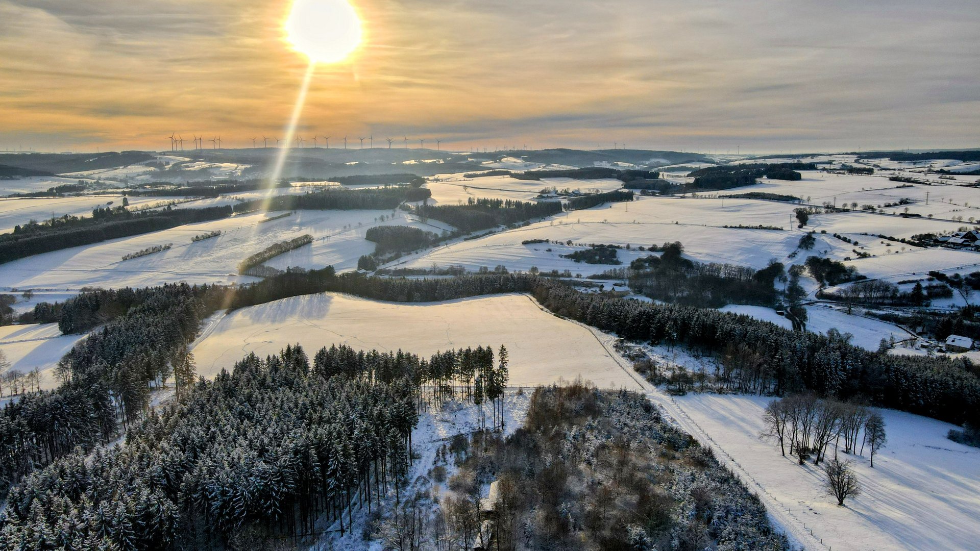 Verschneite Felder und Wälder im Abendlicht, aufgenommen aus der Luft