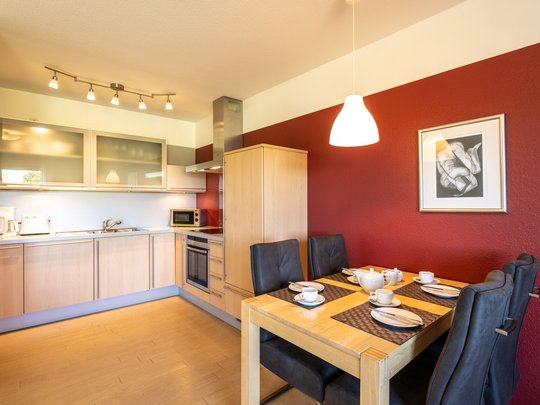 Ihre Unterkunft in Gemünd – Eifel-Urlaub voller Freiheit Moderne Küche mit Holzmöbeln, roter Wand und gedecktem Esstisch