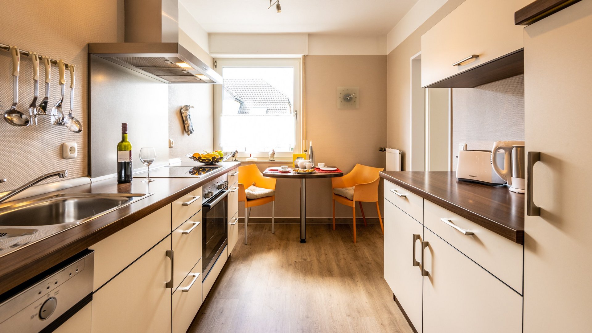 Ihre Unterkunft in Gemünd – Eifel-Urlaub voller Freiheit Moderne Küche mit Esstisch, zwei orangenen Stühlen, Weinflasche und Küchengeräten