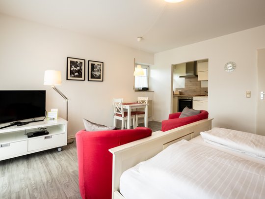 Ihre Unterkunft in Gemünd – Eifel-Urlaub voller Freiheit Helle Einzimmerwohnung mit Bett, roten Sesseln, Fernseher, Esstisch und kleiner Küche
