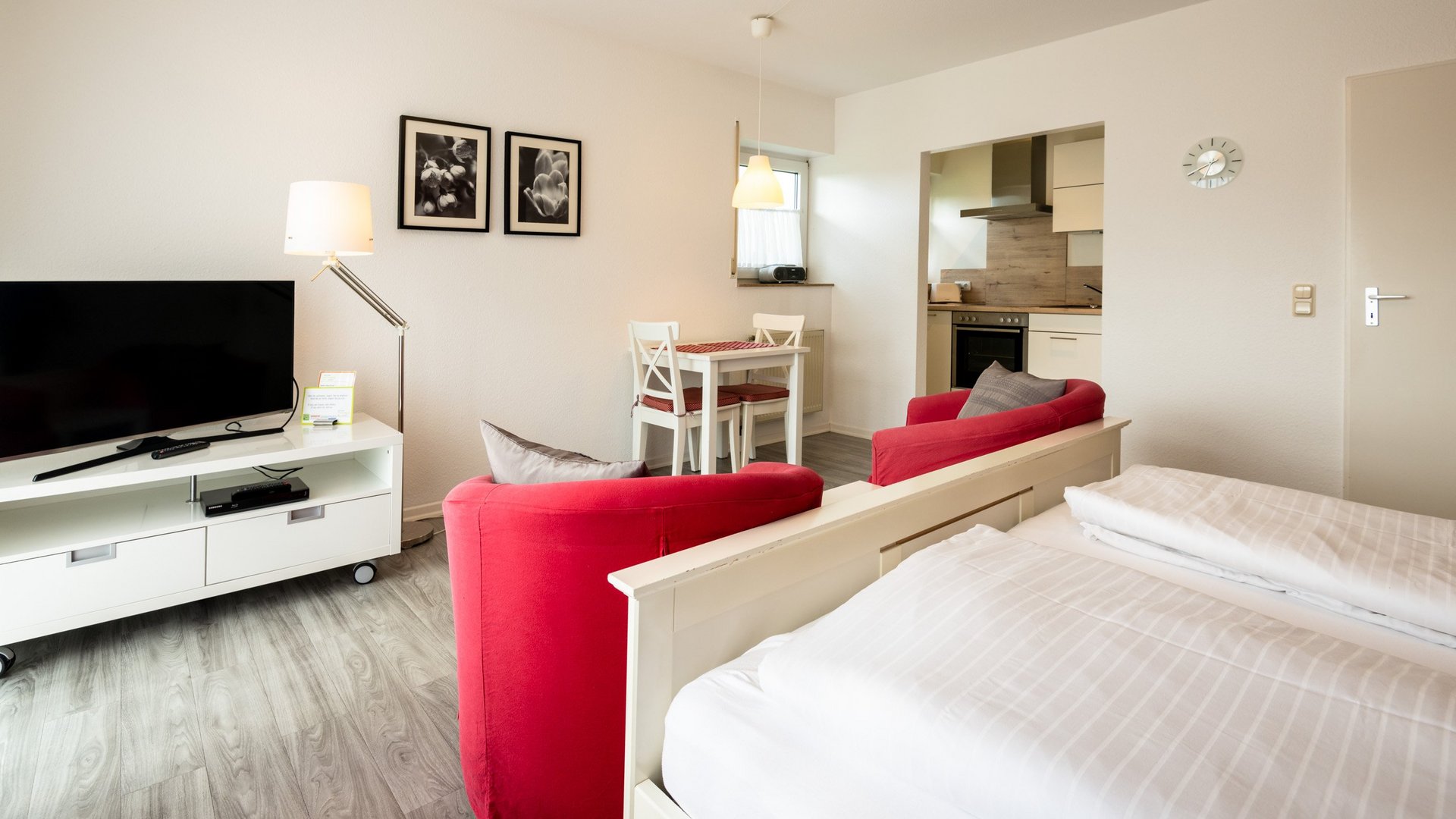 Ihre Unterkunft in Gemünd – Eifel-Urlaub voller Freiheit Helle Einzimmerwohnung mit Bett, roten Sesseln, Fernseher, Esstisch und kleiner Küche