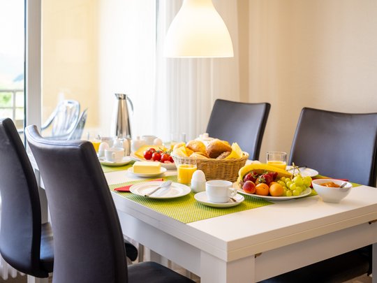 Holiday apartments in Gemünd with special flair Breakfast table with rolls, fruit, eggs, juice, and coffee in modern dining room
