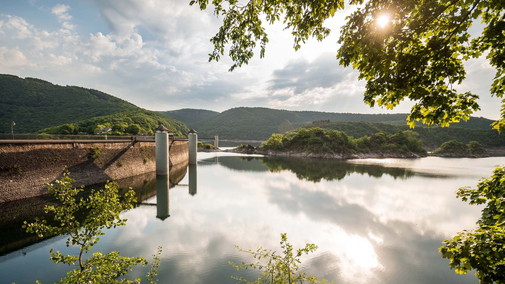 Eifel-Urlaub: Insidertipps aus Gemünd Staumauer mit Wasser und bewaldeten Hügeln unter bewölktem Himmel