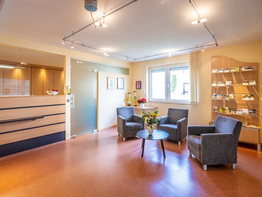 Holiday apartments in Gemünd with special flair Waiting area with three chairs, flowers on table, reception desk, and brochures
