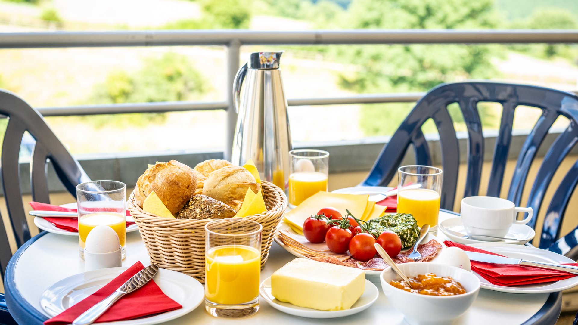Holiday apartments in Gemünd with special flair Table with breakfast on balcony including rolls, cheese, tomatoes, butter, eggs, and orange juice