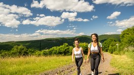 Autumn Short Break in the National Park | Gemünder Ferienpark Two young women hiking on a trail with green hills and blue sky in the background