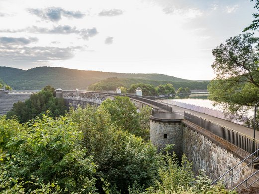 5 Tage Eifel Stauseemauer mit Bäumen im Vordergrund und Hügeln im Hintergrund bei Sonnenuntergang