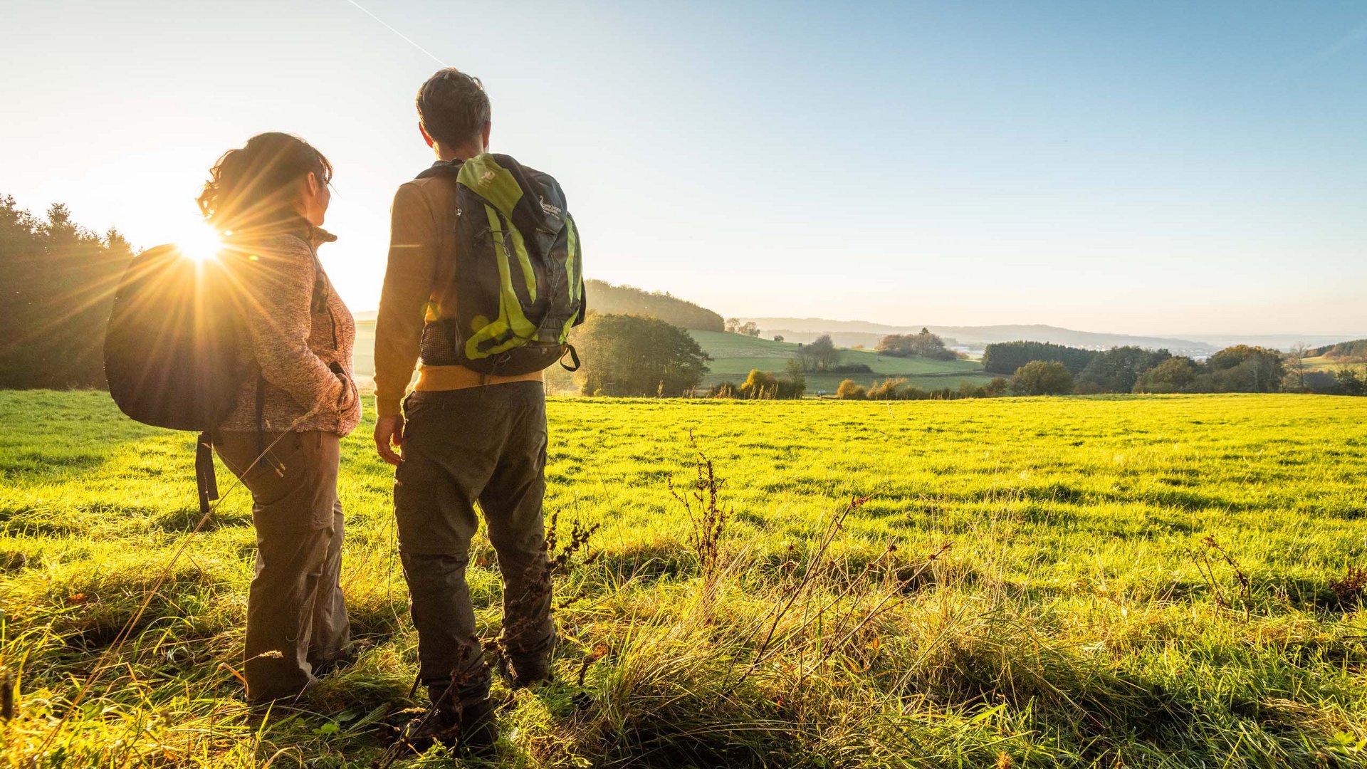Holiday apartments in Gemünd with special flair Two hikers with backpacks looking at a green landscape at sunset
