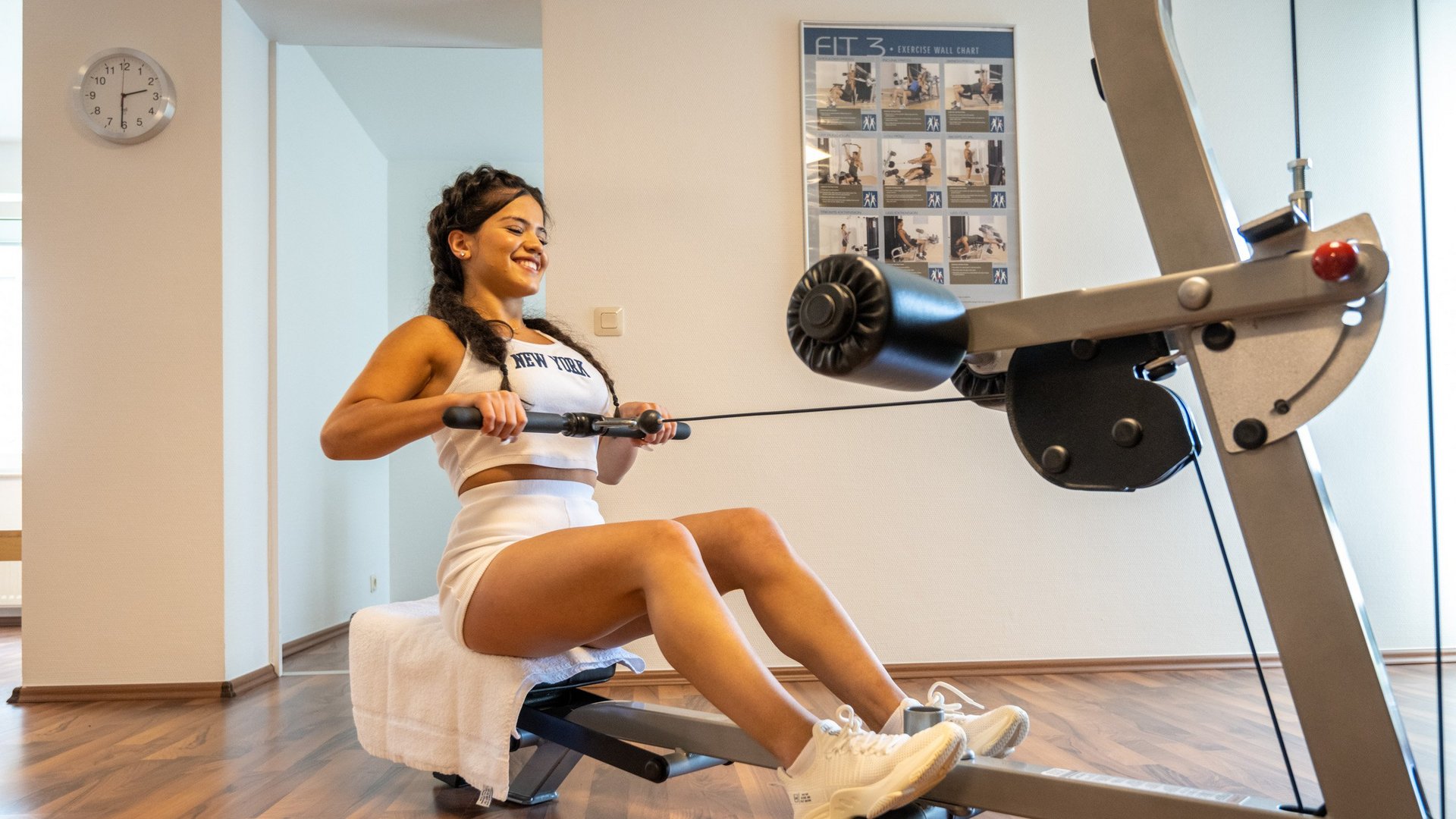 A holiday apartment in the Eifel region with a sauna and gym Woman exercising on rowing machine in bright gym with exercise chart on wall
