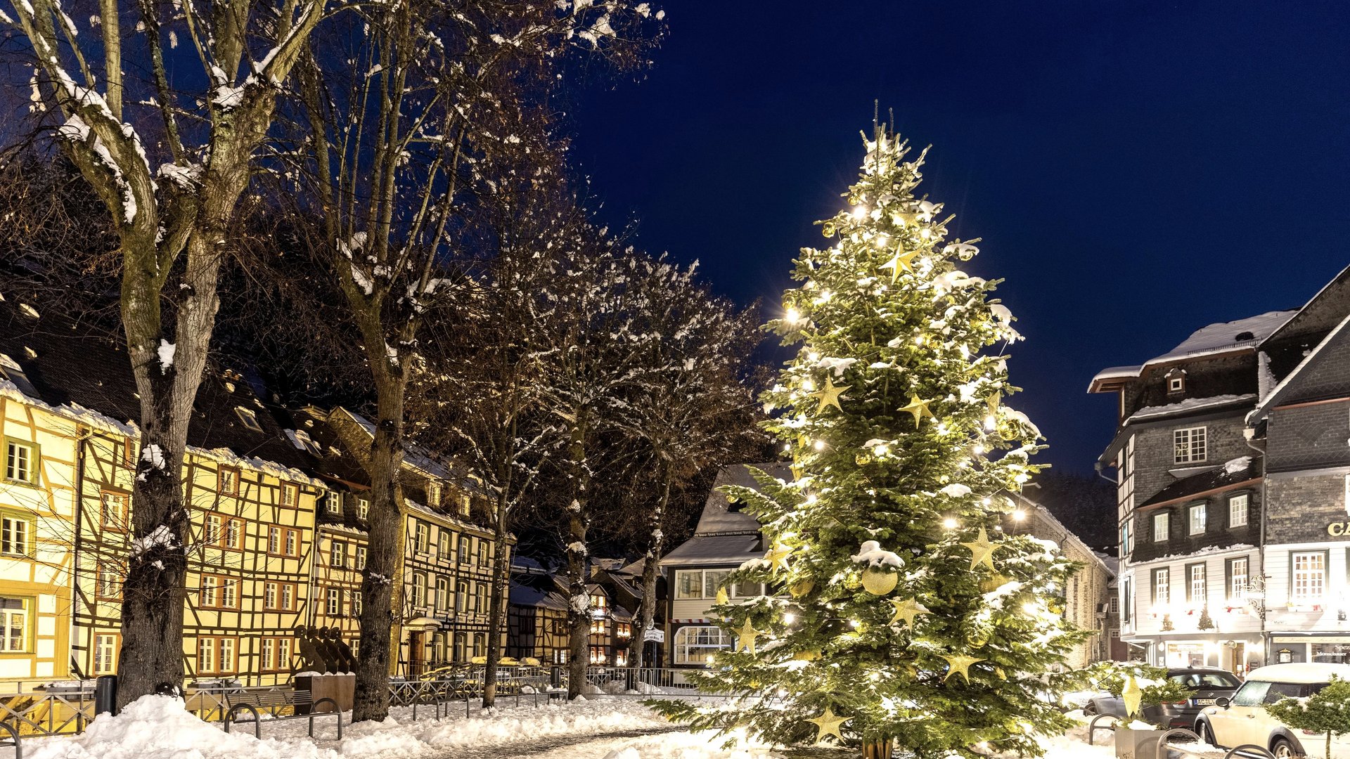 Eifel-Urlaub: Weihnachtsmärkte der Region Beleuchteter Weihnachtsbaum auf verschneitem Platz in historischem Dorf bei Nacht