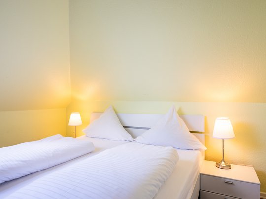 Ihre Unterkunft in Gemünd – Eifel-Urlaub voller Freiheit Gemütliches Schlafzimmer mit weißem Bett, zwei Kissen und zwei Nachttischlampen