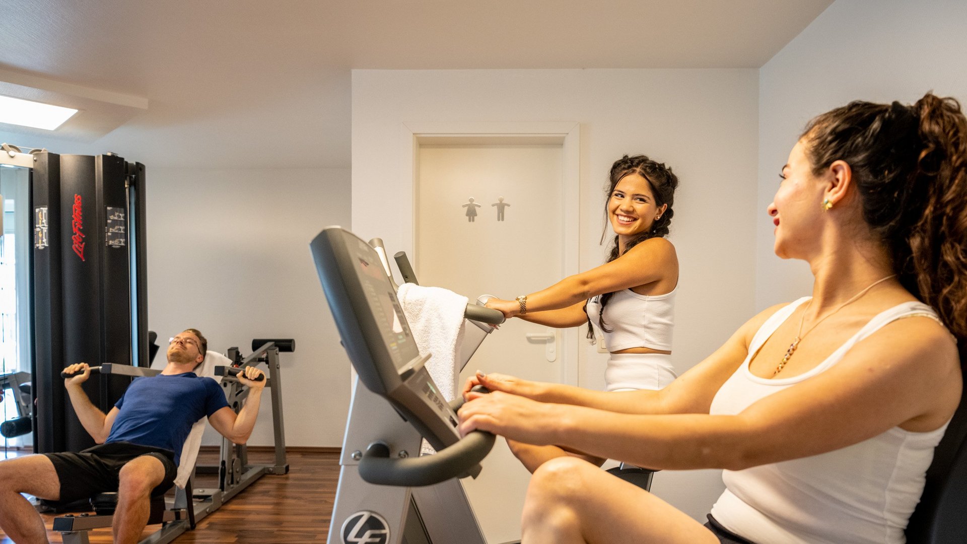 Urlaub in der Eifel mit Hund? Aber natürlich! Drei Personen trainieren in einem Fitnessstudio an verschiedenen Geräten.