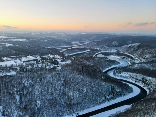 Herbst und Winterzauber in der Eifel genießen Winterlandschaft mit verschneiten Hügeln, Flusslauf und Gebäuden bei Sonnenuntergang